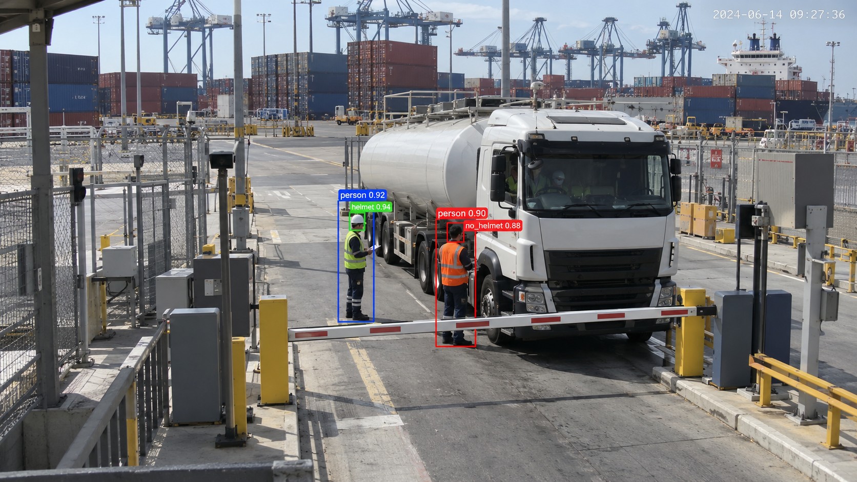 Detection view of a tanker truck stopped at a port gate barrier, one worker boxed as person and helmet and the other flagged as no_helmet