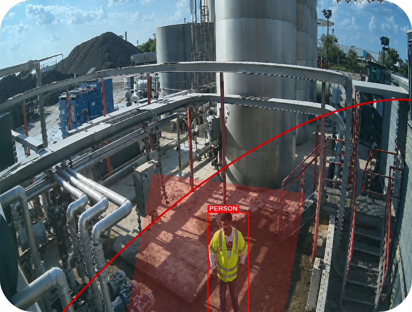 Worker in a high-visibility vest detected and boxed inside a shaded red restricted zone at a bitumen plant, with the geofence boundary drawn across the walkway