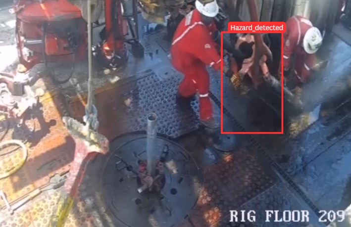 Rig floor camera feed with workers and a hazard boxed and labelled Hazard_detected near the drill pipe